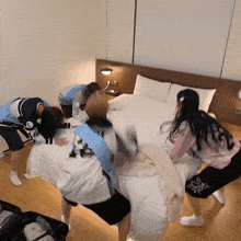 a group of girls are playing with pillows on a bed in a room