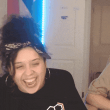 a woman wearing a bandana and hoop earrings laughs with her eyes closed