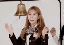a girl in a school uniform stands in front of a brass bell