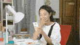 a woman is sitting at a desk looking at a cell phone with kbs2 written on the door behind her
