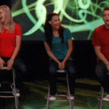 a group of people are sitting on stools in front of a screen with the letter g on it