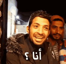 a man in a fur hooded jacket is smiling with arabic writing on his face .