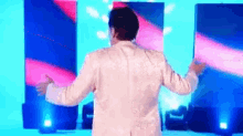 a man in a white suit is standing on a stage with his arms outstretched in front of a screen .