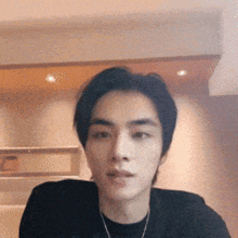 a young man wearing a black shirt and a necklace is sitting in a room .