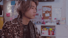 a young man wearing a leopard print cardigan looks to the side