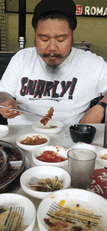 a man wearing a shirt that says " gnarly " is eating food