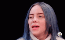 billie eilish with blue hair is making a funny face with her mouth open .