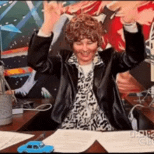 a woman is sitting at a desk with her arms in the air and smiling .