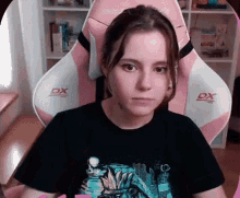 a woman is sitting in a pink and white dx gaming chair .