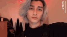 a young man with gray hair and earrings is taking a selfie in a room .