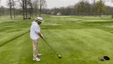a man wearing a hat is swinging a golf club on a golf course