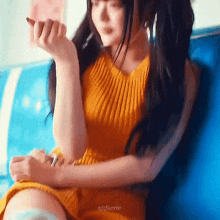 a woman in a yellow dress is sitting on a blue couch holding a pen .