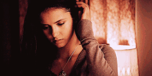 a woman adjusts her hair while wearing a necklace and a sweater