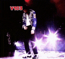 a man in a blue jacket is dancing on a stage in front of a sign that says " v103 "