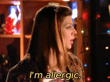 a woman says " i 'm allergic " while standing in front of christmas lights