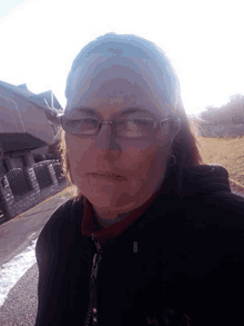a woman wearing glasses and a black jacket looks at the camera