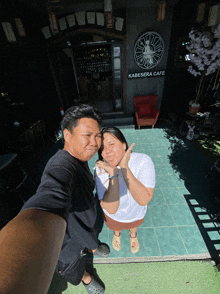 a man and a woman are posing for a picture in front of a kabesara cafe