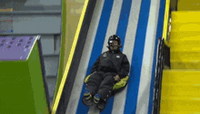 a person wearing a 3m helmet is sliding down a blue and white striped slide