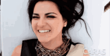 a woman is smiling and wearing a necklace that says caras on the bottom
