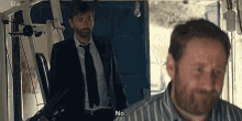 a man in a suit and tie is standing next to another man in a striped shirt and saying no .