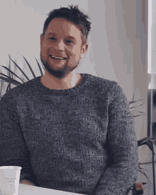 a man in a grey sweater sits at a table with a cup that says bob elliot coffee