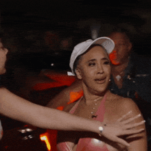 a woman wearing a white hat and a pink top is hugging another woman