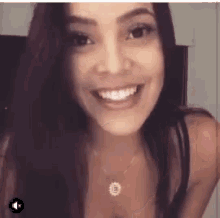 a woman with long dark hair is smiling and wearing a necklace with the letter e on it .