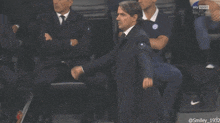 a man in a suit and tie holds his fist in the air while watching a sports game on sky sport