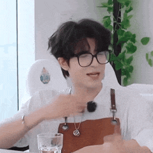 a young man wearing glasses and an apron is sitting at a table with a glass of water in front of him .