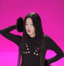 a woman in a black top holds her hair in a ponytail on a pink background