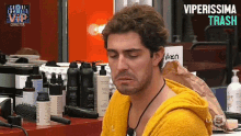 a man in a yellow robe is sitting in front of a table with bottles of shampoo and conditioner .