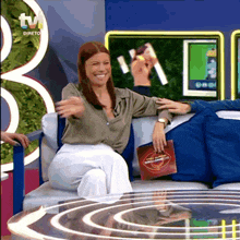a woman is sitting on a couch in front of a tv holding a magazine that says ' direto ' on it