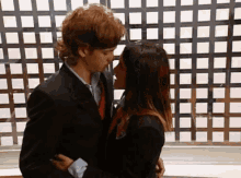 a man and a woman are kissing in front of a wall with squares