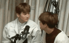 two young men are talking to each other in front of a microphone in a room .