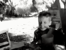 a black and white photo of a young boy sitting in front of a bag of food .