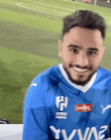 a man with a beard is wearing a blue jersey and smiling .