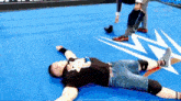 a man is laying on the floor in a wrestling ring while a referee looks on .
