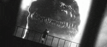 a black and white photo of a woman standing on a balcony looking at a monster .