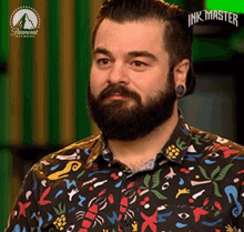 a man with a beard and piercings is wearing a colorful shirt and looking at the camera .