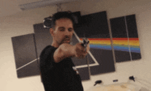 a man is pointing a gun in front of a painting of a rainbow
