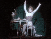 a woman is sitting at a table with her arms outstretched .