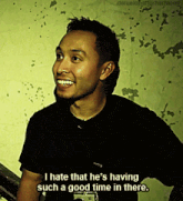a man in a black shirt is smiling and saying i hate that he 's having such a good time in there