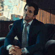 a man in a suit and tie is sitting with his hands folded