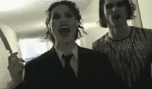 a man in a suit and tie is holding a knife next to a woman .