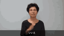 a woman wearing glasses and a black shirt is making a gesture with her hand .