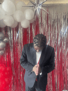 a man in a tuxedo stands in front of a red and silver tinsel curtain