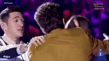 a man in a yellow jacket is hugging another man in front of maestros de la costura