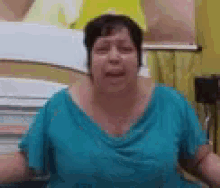 a woman in a blue shirt is making a funny face while sitting in a room .