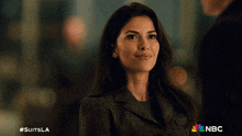 a woman in a suit is smiling with the nbc logo in the corner