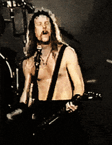 a shirtless man is singing into a microphone while playing a guitar